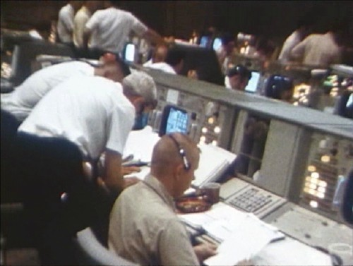 Flight controllers leaning over consoles during the Apollo 11 lunar descent, headsets on, screens glowing.