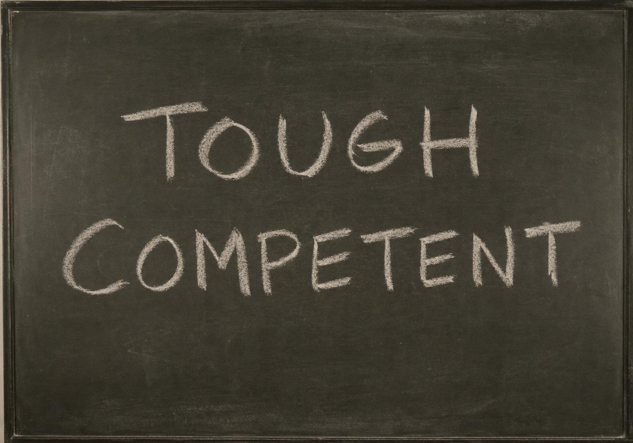 A classroom blackboard with the words TOUGH and COMPETENT written in white chalk.
